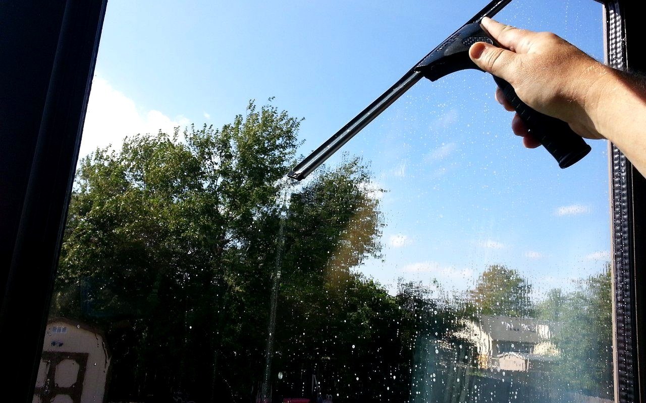 First-person view of a squeegee mid-pass on a residential window, blue sky beyond